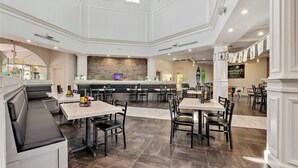 Un restaurant spacieux avec de hauts plafonds, un bar central et différents types de sièges, notamment des banquettes et des tables.