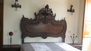 Un dormitorio con un cabecero de madera grande y decorativo, una cama con colchón blanco, dos mesitas de noche y apliques de pared.