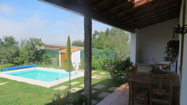 Un patio techado con piscina, un pequeño jardín y una mesa con sillas.