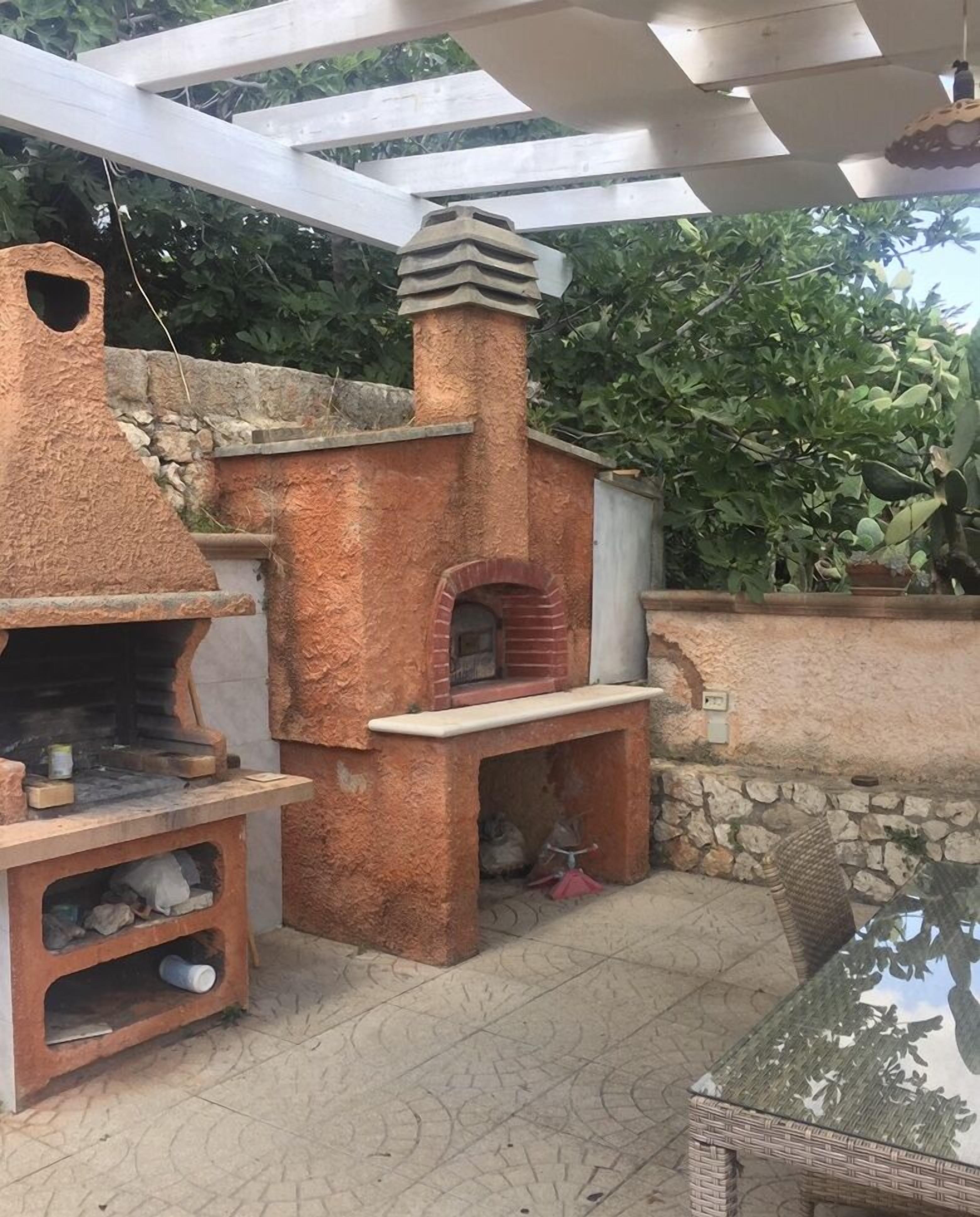 An outdoor kitchen area with a brick oven, a stone wall, and a pergola.