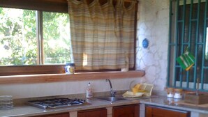 A kitchen with wooden cabinets, a gas stove, a sink, and a window with a plaid curtain. - Castro: House with private access to the sea (Castro)