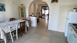 A spacious kitchen with a dining area, featuring a tiled floor, a white refrigerator, and a cabinet with glass doors. - Villa Lido di Spina "Adriatic coast" (Lido di Spina)