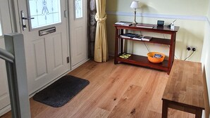 Ett rum med trägolv, en dörr med glaspaneler, ett skrivbord med en lampa, en bokhylla och en tavla på väggen.