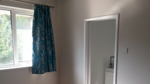 Ett sovrum med en säng, ett fönster med gardiner, en dörr som leder till ett badrum och en liten matta på golvet.