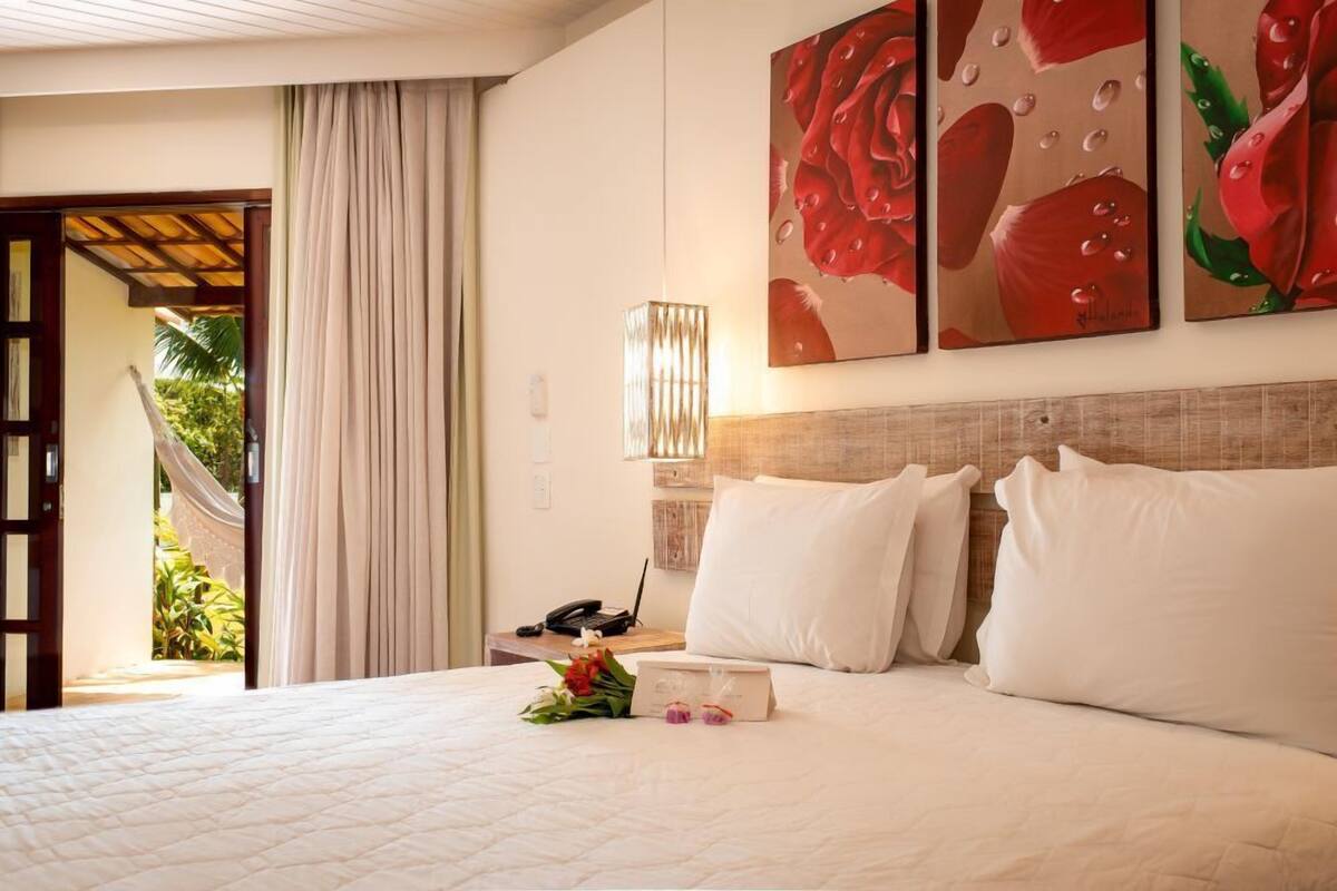 A hotel room with a bed, a nightstand, a lamp, and a painting of roses.