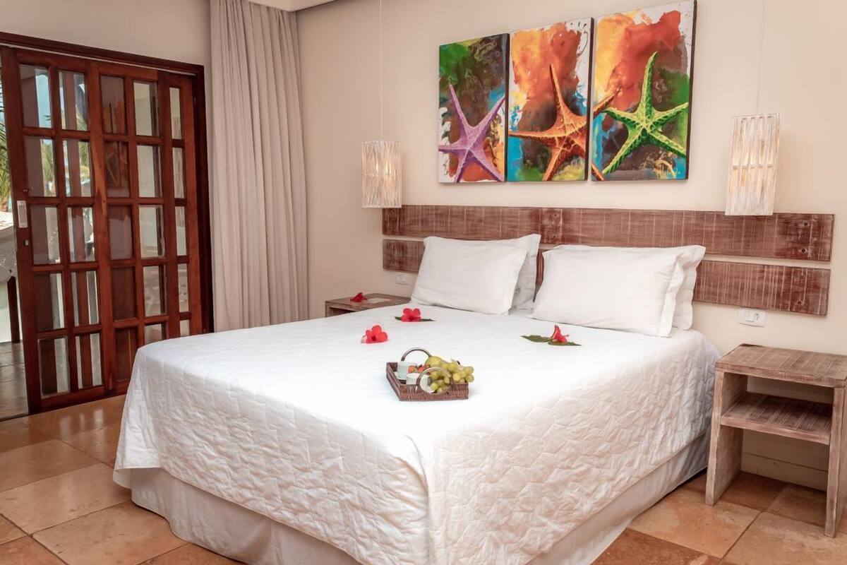 A hotel room with a large bed, a wooden headboard, a nightstand, a wall-mounted lamp, and a door with glass panels.