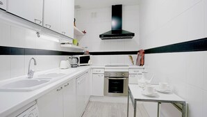 Una cocina moderna con armarios blancos, un lavamanos de acero inoxidable, un microondas, una tetera y una cafetera sobre una mesita.