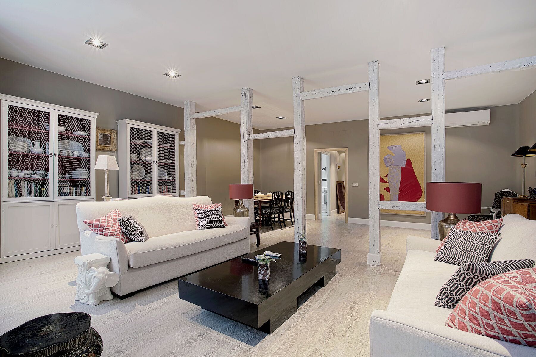 A spacious living room with a white sofa, a black coffee table, and a dining area with a wooden table and chairs.