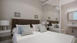 Una habitación de hotel con una cama grande, dos mesitas de noche con lámparas, un espejo y un baño con lavamanos y ducha.