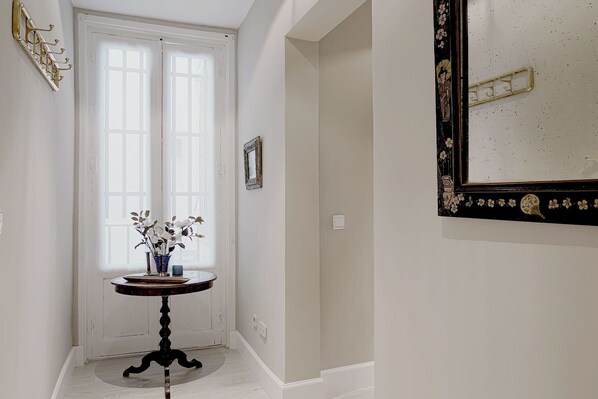 A hallway with a white door, a small table with a vase of flowers, and a mirror with a decorative frame. - Genteel Home Huertas (Madrid)