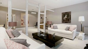 Una sala de estar moderna con un sofá blanco, una mesa de centro negra y un sillón blanco. Hay un cuadro en la pared y una lámpara sobre una mesita auxiliar.