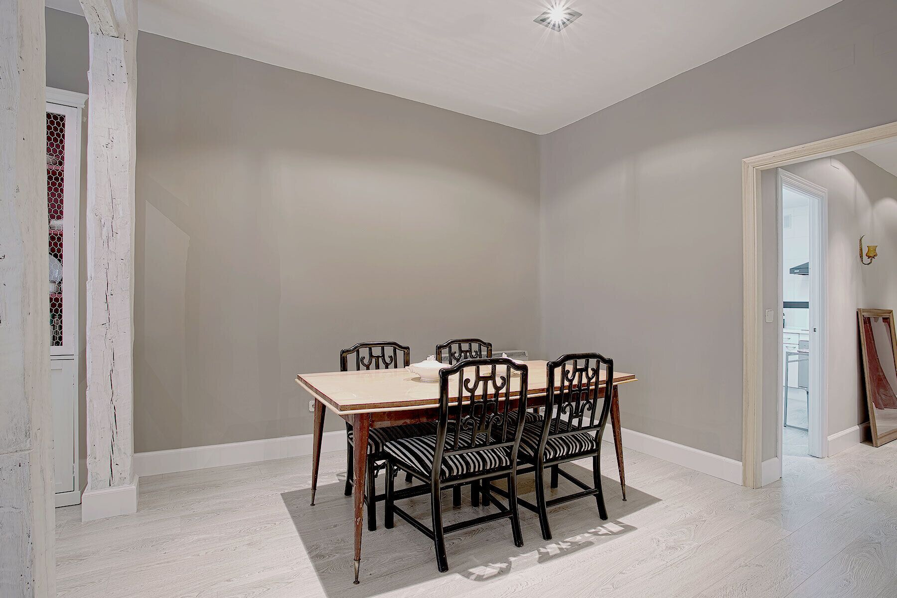 Un comedor con una mesa rectangular y cuatro sillas, una puerta blanca y un pasillo que conduce a otra habitación.