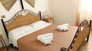A bed with a brown quilt, white pillows, and rolled towels on the side. - Residenza I Filari: a villa surrounded by greenery. (Alghero)