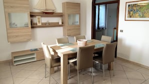 A dining area with a wooden table, six chairs, a hanging light fixture, and a view through an arched doorway. - Residenza I Filari: a villa surrounded by greenery. (Alghero)