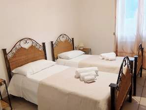Ein Hotelzimmer mit drei Einzelbetten, jeweils mit Kopfstütze, weißer Bettwäsche und zusammenrollten Handtüchern auf den Betten.