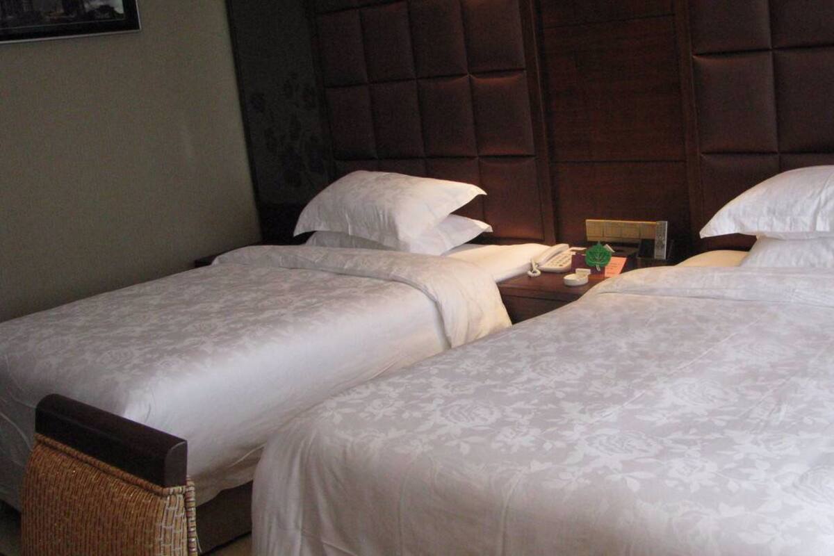 Une chambre d’hôtel avec deux lits simples, une tête de lit en bois, une table de chevet avec un téléphone et une petite plante verte.
