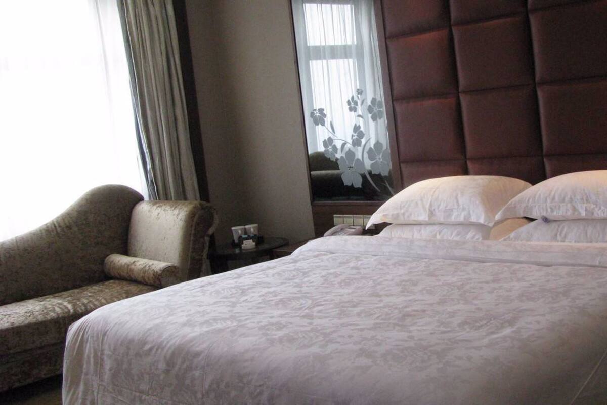 Une chambre d’hôtel avec un grand lit, une chaise, une table de chevet et une fenêtre avec des rideaux.