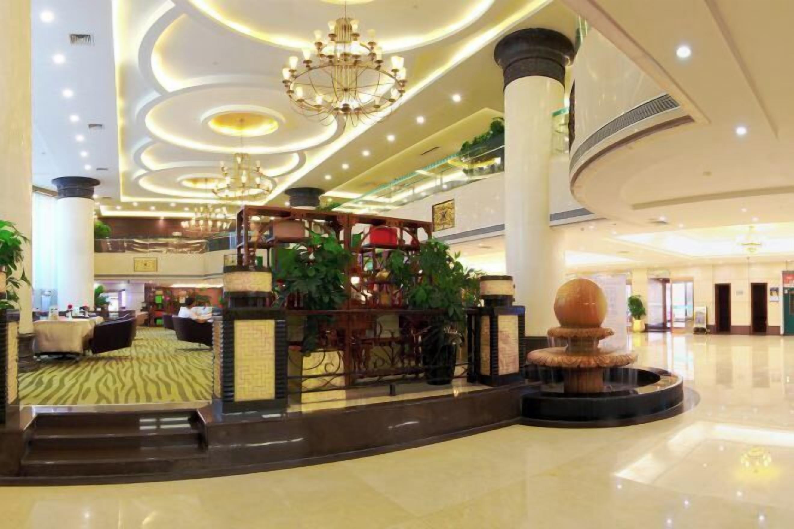 A spacious lobby with a central fountain, multiple seating areas, and a high ceiling with circular lighting.
