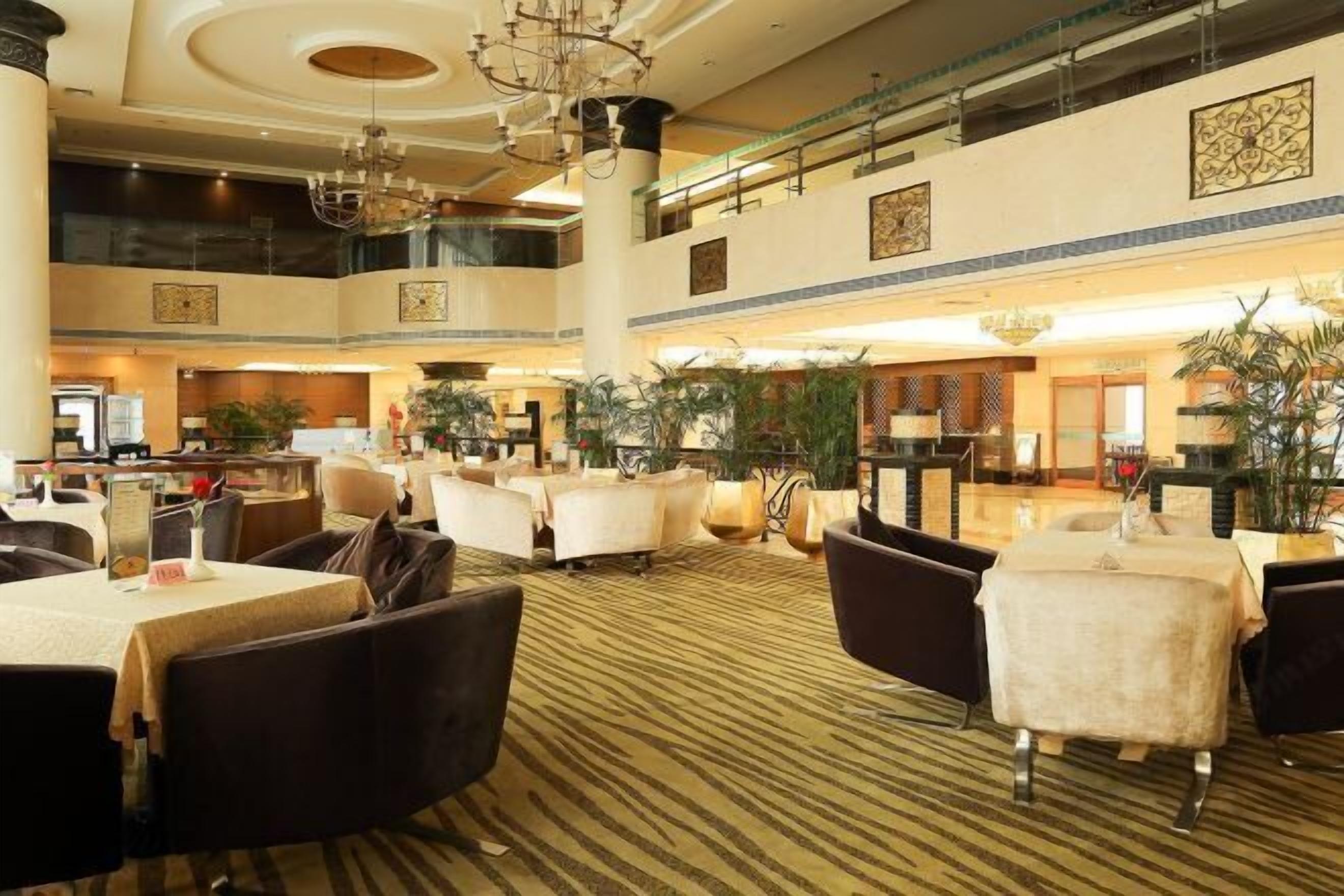 Un amplio vestíbulo de hotel con varias zonas de restauración, asientos cómodos y plantas decorativas.
