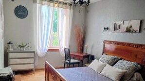A bedroom with a bed, a desk, a chair, a dresser, and a window with curtains.