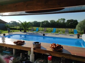 Zona de piscina con sillones de descanso y una mesa con comida y bebidas.