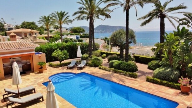 A swimming pool with lounge chairs and umbrellas, surrounded by palm trees and a view of the sea. - Experience Ultimate Luxury and Convenience at our 5-Star Villa with Private Pool (Teulada, Moraira)