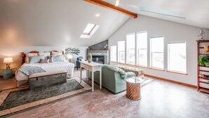 A spacious bedroom with a large bed, a desk, and a sofa. There is a fireplace and a skylight. - Whitewater Ocean View, Spa, Secret Game Room, 800 SF Master Suite (Newport)
