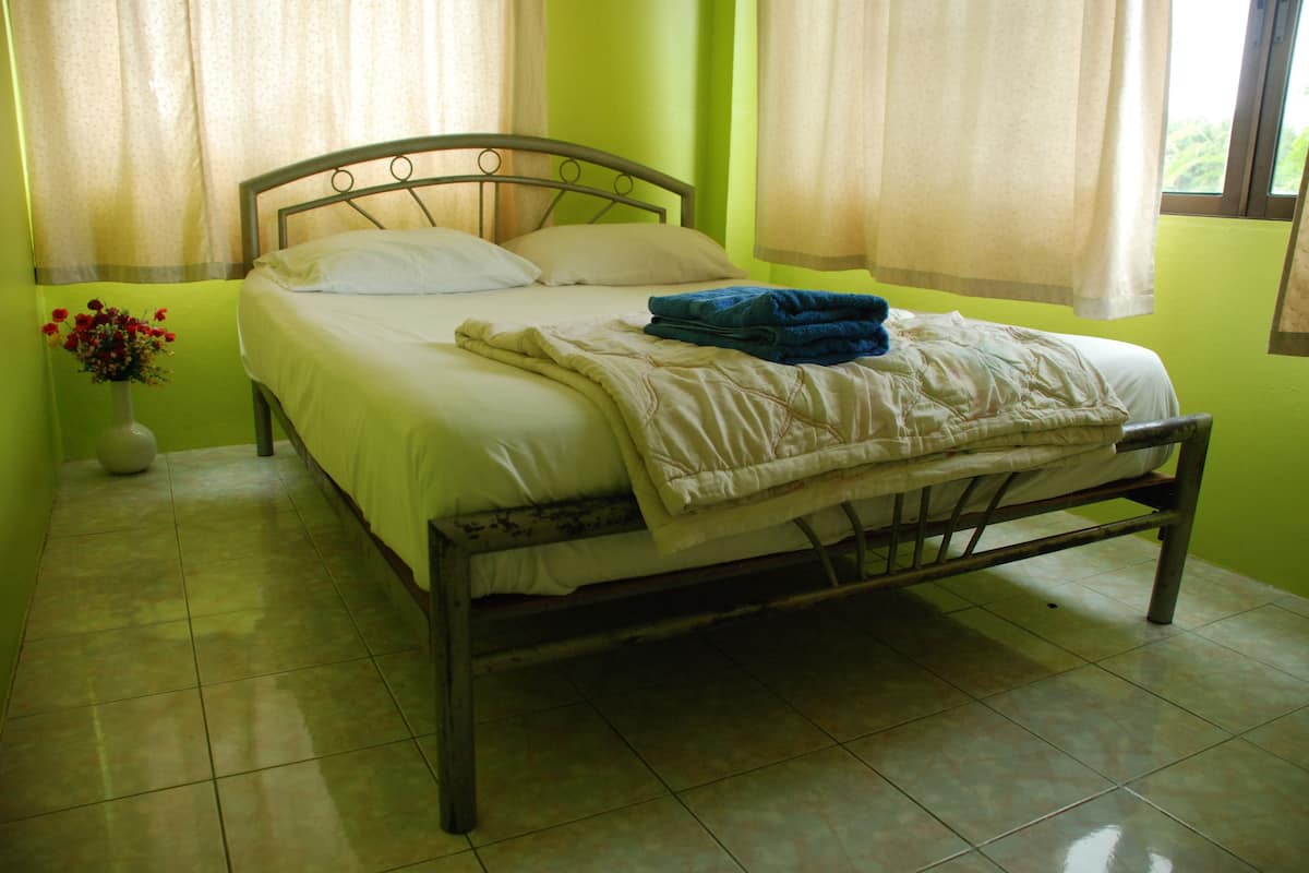 Un lit avec un cadre en métal, une couvre-lit blanche et une couverture bleue pliée sur le dessus.