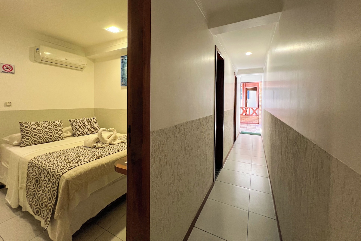 A hotel room with a bed, a bedside table, and a wall-mounted air conditioner.