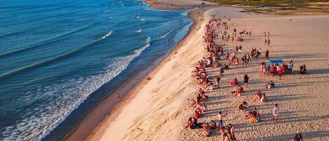 Una playa con gente tomando el sol y nadando, cielo despejado y un pueblo lejano.