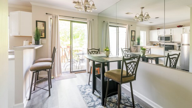 A dining area with a table and chairs, a kitchen with appliances, and a large mirror reflecting the space.
