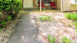A house with a stone facade, a covered porch with two red chairs, and a pathway leading to the front door.