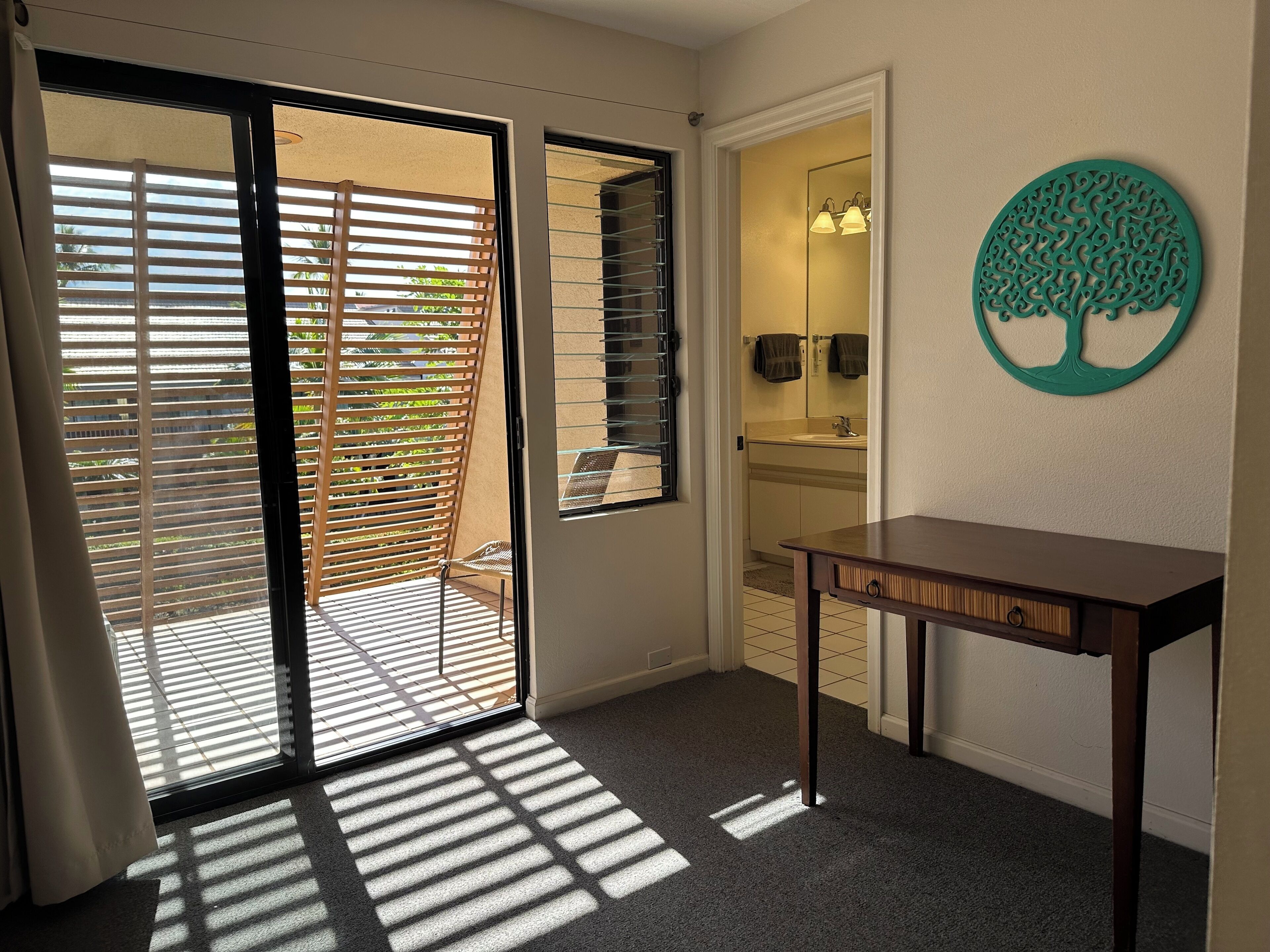 Une pièce dotée d’une porte-fenêtre coulissante donnant sur un balcon, d’une petite table et d’un élément décoratif fixé au mur.