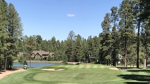 Un campo de golf con un estanque, árboles y un edificio al fondo.