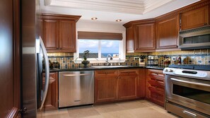 A kitchen with wooden cabinets, stainless steel appliances, and a view of the ocean.