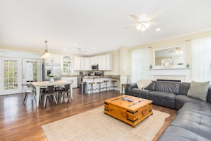 A spacious living room with a dark leather sofa, a wooden coffee table, and a dining area with a white table and chairs.