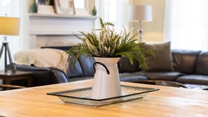 Een witte keramieken vaas met handvat op een glazen dienblad, geplaatst op een houten tafel in een woonkamer.