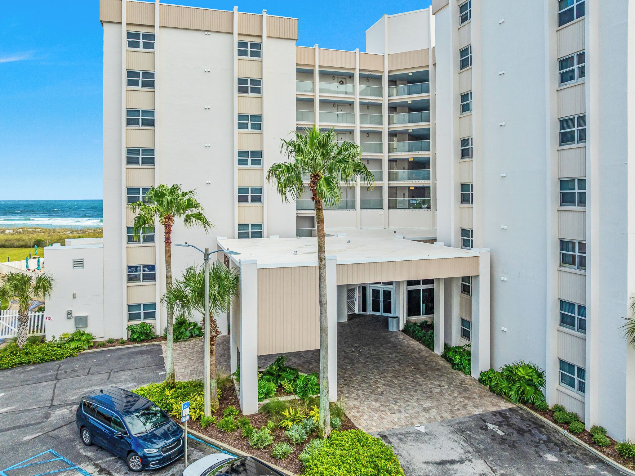 Ein mehrstöckiges Hotel mit flachem Dach, Palmen und einem Parkplatz.