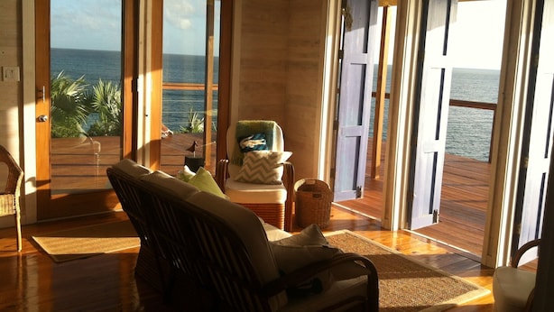 Una habitación con vista al océano, una silla, una mesita pequeña y una cesta de mimbre.