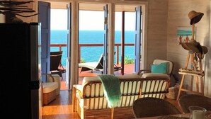 Amplia sala de estar con vista al mar, piso de madera y ventilador de techo.