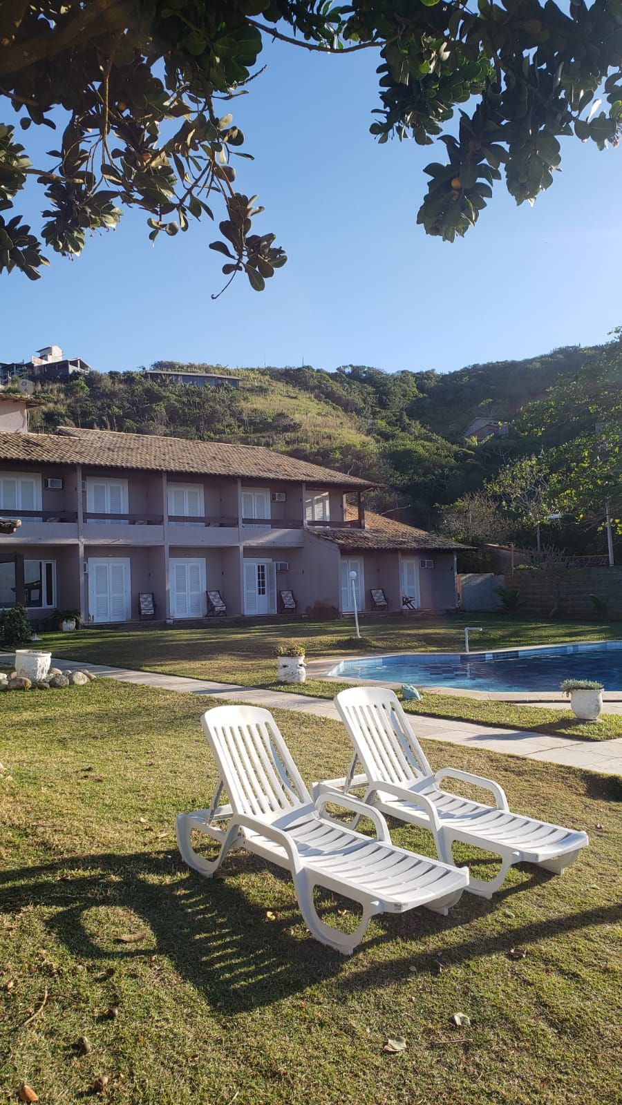 A hotel with a swimming pool, white lounge chairs, and a view of the surrounding hills.