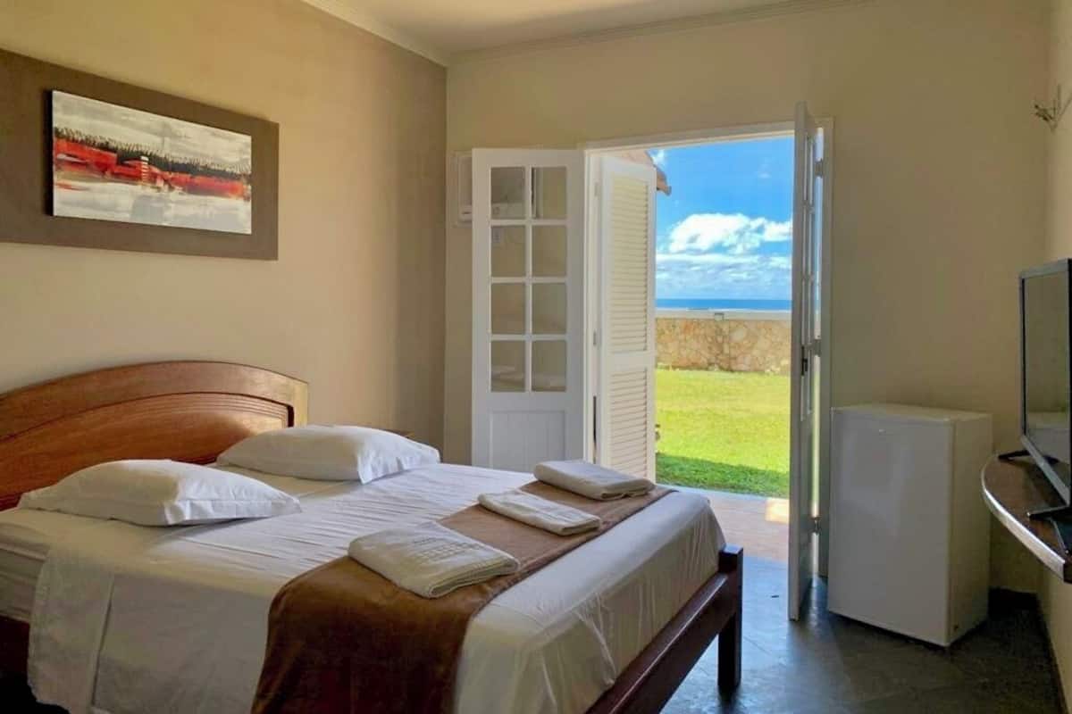 A hotel room with a bed, a television, and a door leading to a balcony with a view of the sky and grass.