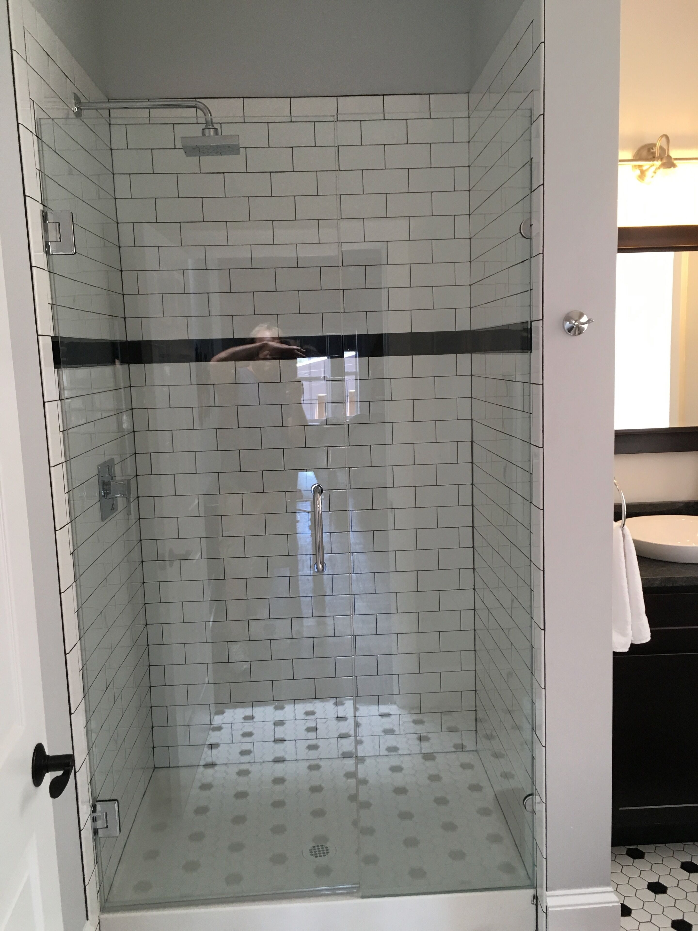 A glass-enclosed shower with a tiled wall, a handrail, and a visible drain.