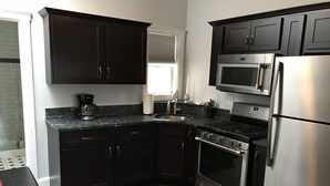 A modern kitchen with dark cabinets, stainless steel appliances, and a wooden floor.