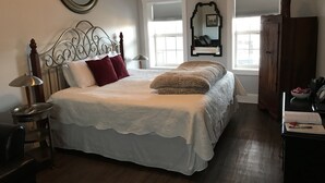 A bedroom with a four-poster bed, a bedside table with a lamp, a wooden wardrobe, and a mirror on the wall.