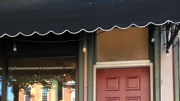 A red door with a mailbox, a window with a view of a building, and a doorbell.