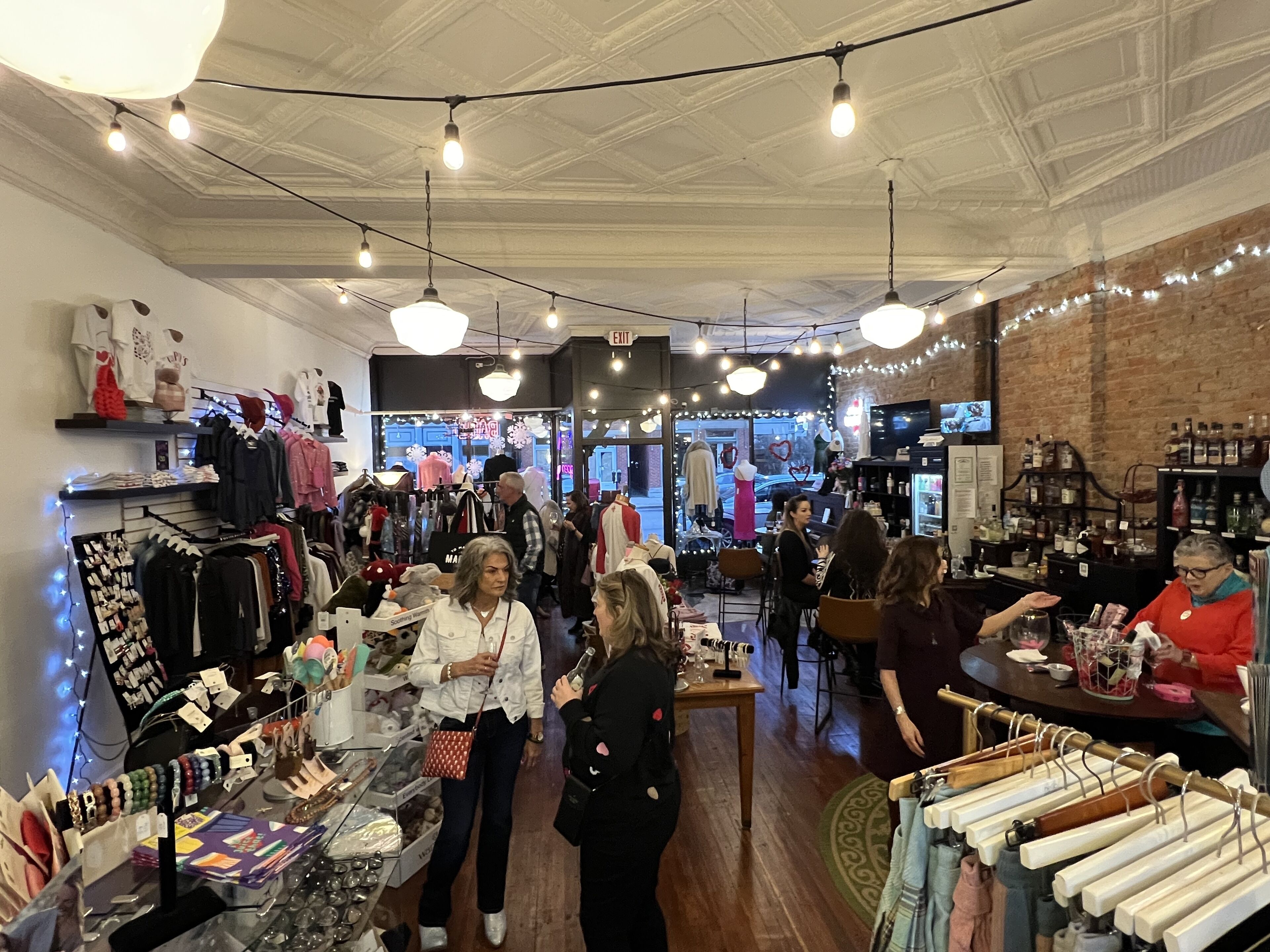 A boutique clothing store with racks of clothes, a jewelry display, and a seating area with tables.