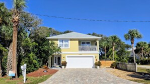 A two-story house with a garage, surrounded by palm trees and a well-maintained lawn. - 1ST STREET II BEACH HOUSE, UPDATED DOG FRIENDLY  FENCED IN YARD 1 BLOCK TO BEACH (St. Augustine)