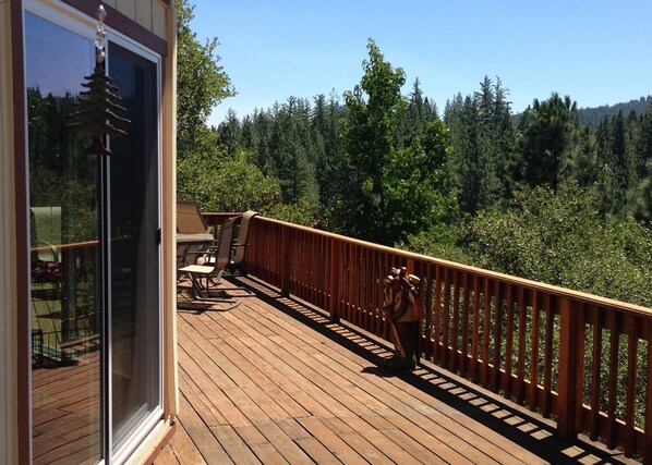 A wooden deck with a glass door, outdoor furniture, and a view of a forested area.