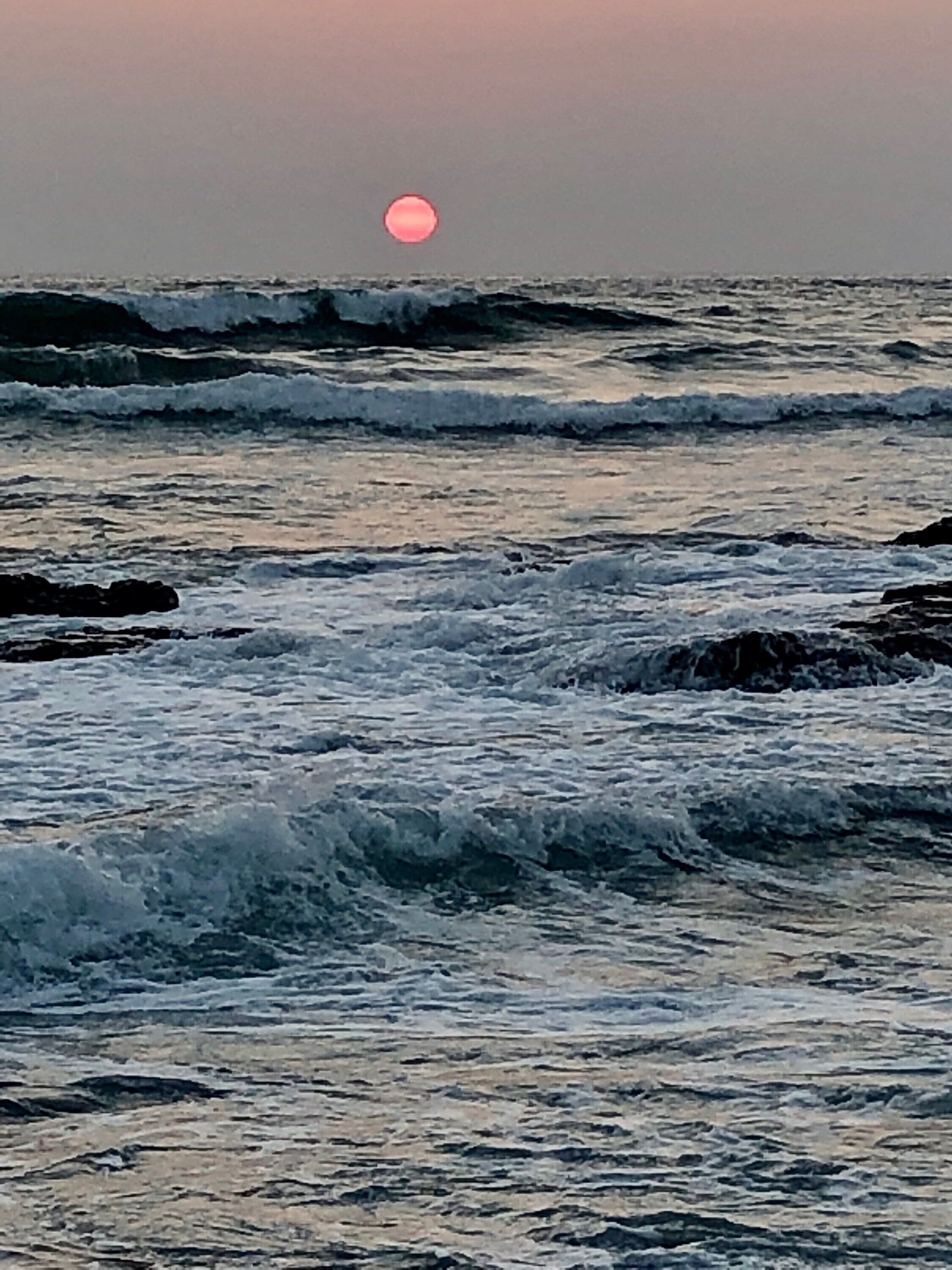 Un atardecer sobre el océano con olas rompiendo sobre las rocas.